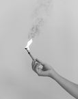 angezündeter Palo Santo Stick mit Flamme in schwarz-weiß wird von Hand gehalten