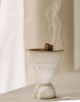 Cone Räuchergefäß aus beigefarbenem Travertinstein mit Palo Santo Stick rauchend während Räucherroutine