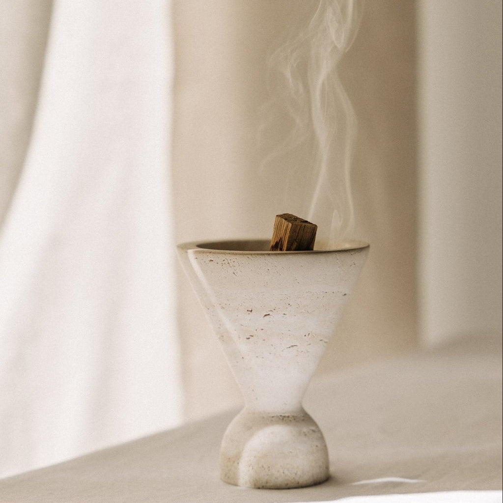Cone Räuchergefäß aus beigefarbenem Travertinstein mit Palo Santo Stick rauchend während Räucherroutine