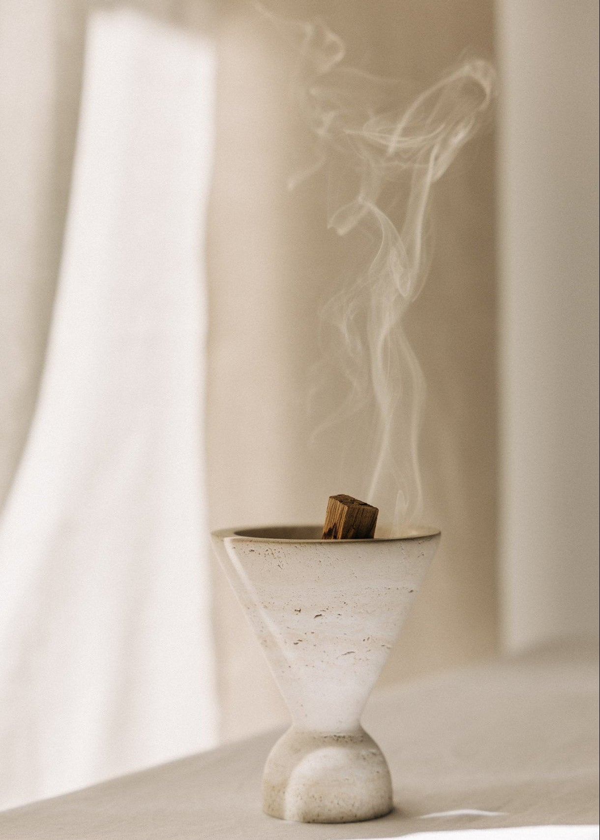 Cone Räuchergefäß aus beigefarbenem Travertinstein mit Palo Santo Stick rauchend während Räucherroutine
