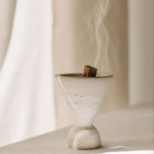 Cone Räuchergefäß aus beigefarbenem Travertinstein mit Palo Santo Stick rauchend während Räucherroutine