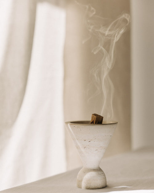 Cone Räuchergefäß aus beigefarbenem Travertinstein mit Palo Santo Stick rauchend während Räucherroutine