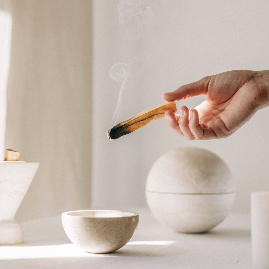 Kleine Räucherschale aus beigefarbenem Travertinstein mit angezündetem Palo Santo Stick im Travertin Räucherbundle